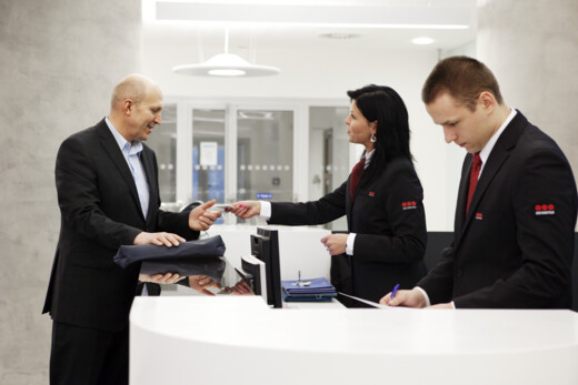 Reception desk at a modern office building where reception staff assist a visitor during check-in, with another staff member updating information at the front desk.