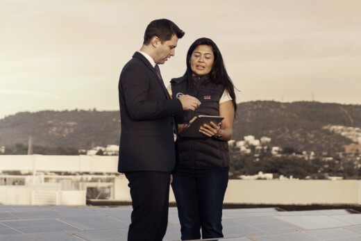 Securitas employees wearing a branded vest stand together on a rooftop looking down at a tablet computer, with solar panels in the foreground and hills in the background.