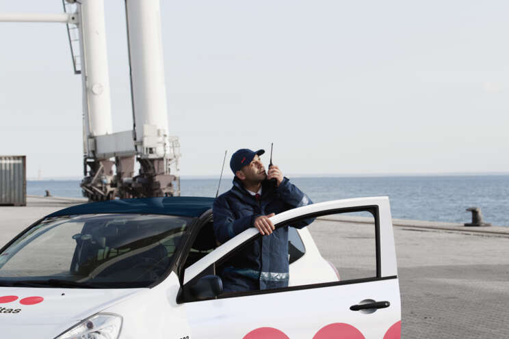 Securitas-vagt står og taler i radio foran sin patruljebil