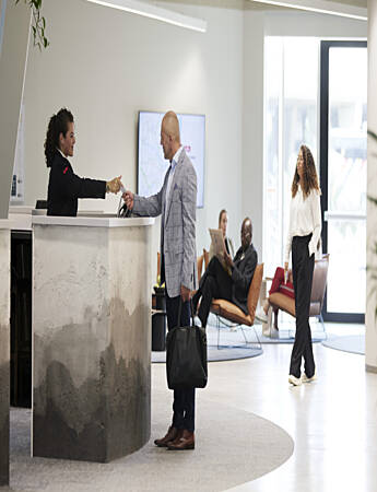 Kvinnelig Securitas-resepsjonsvekter bistår en besøkende mann i et kontorbygg.