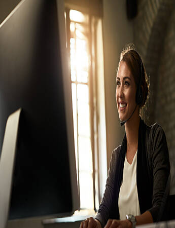 Person wearing a headset and seated at a desk, working on a computer in an office environment.