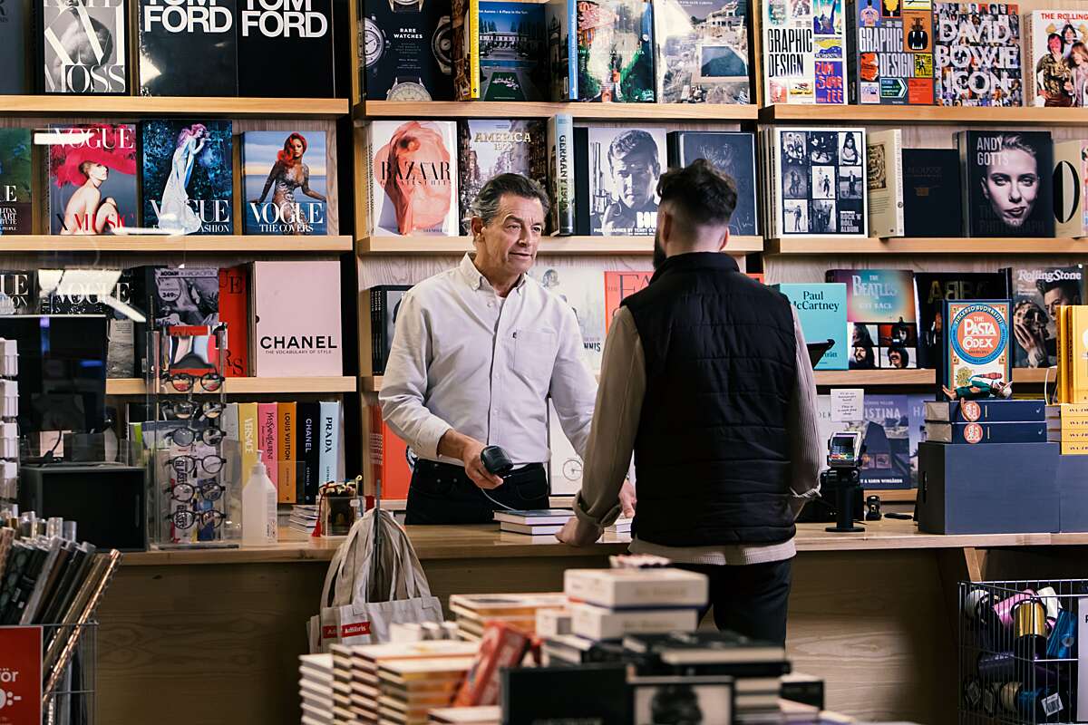 Ekspedienten i en butik, der sælger bøger, taler med en kunde ved kassen