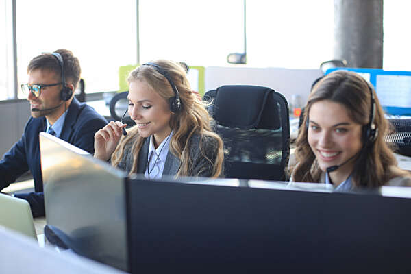 Female customer support operator with headset and smiling, with colleagues at background