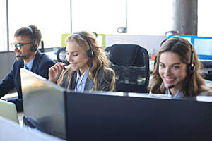 Female customer support operator with headset and smiling, with collegues at background