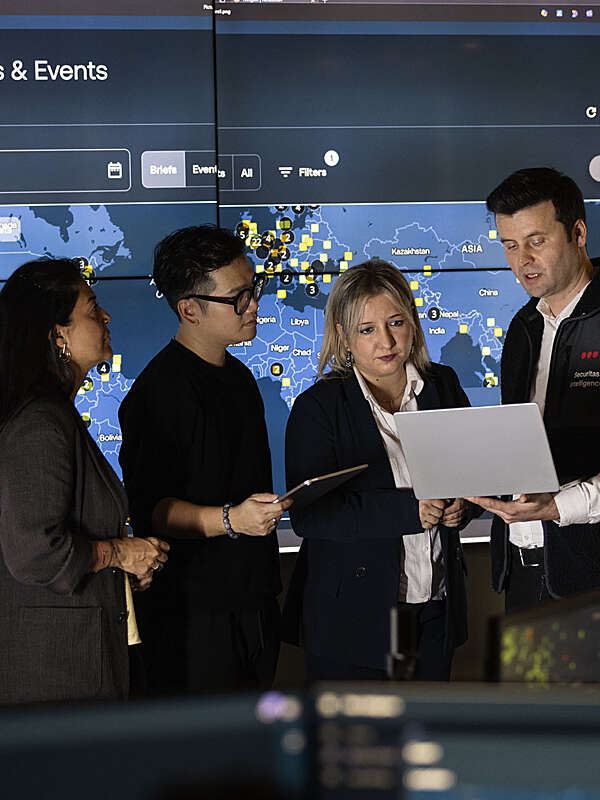 Four Securitas analysts standing in front of large screens while looking at a laptop.