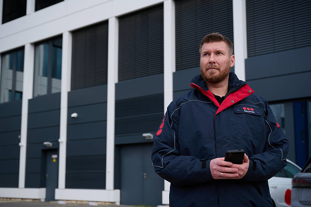 Securitas security officer using a mobile device to manage security operations outside a commercial building.