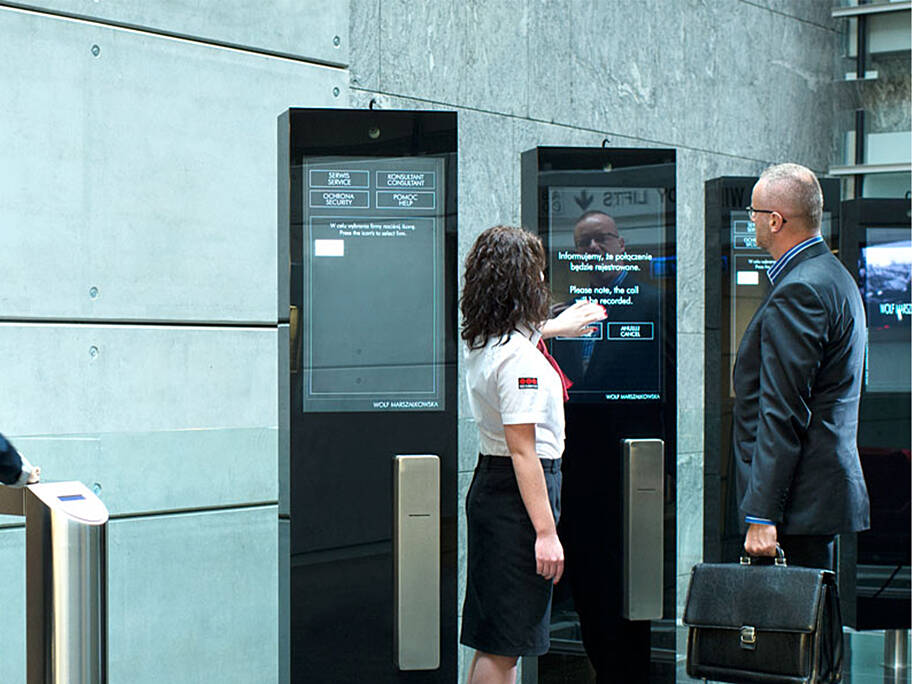 Visitor using a digital visitor management kiosk while a Securitas security officer provides assistance in a modern office building reception area.