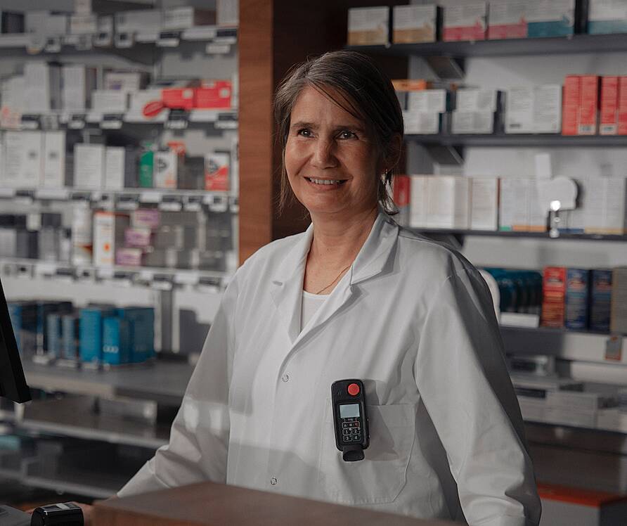 Pharmacy employee wearing a Securitas Lone Worker device on the shop floor.