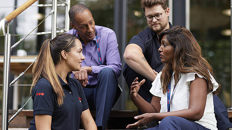 2 weibliche Securitas Mitarbeiterinnen und zwei männliche sitzen auf einer Stiege und unterhalten sich
