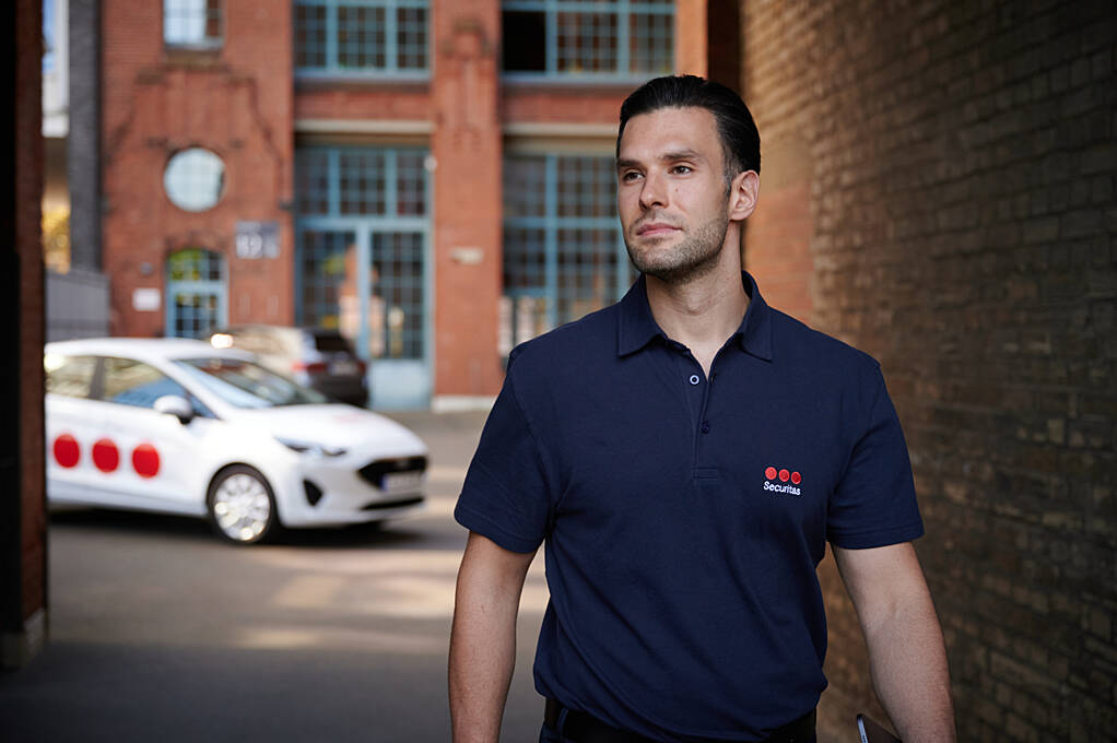 Security guard is walking near guarded building with Securitas patrol car on the background