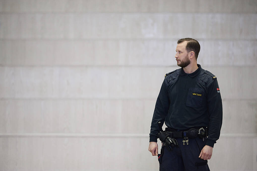 Securitas biztonsági munkatárs egyenruhában, beltéri környezetben áll, élőerős helyszíni szolgáltatások keretében biztosítva a terület védelmét.