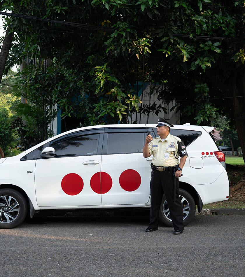 Securitas mobile guard standing next to a company patrol car, opening the vehicle door outside a building.