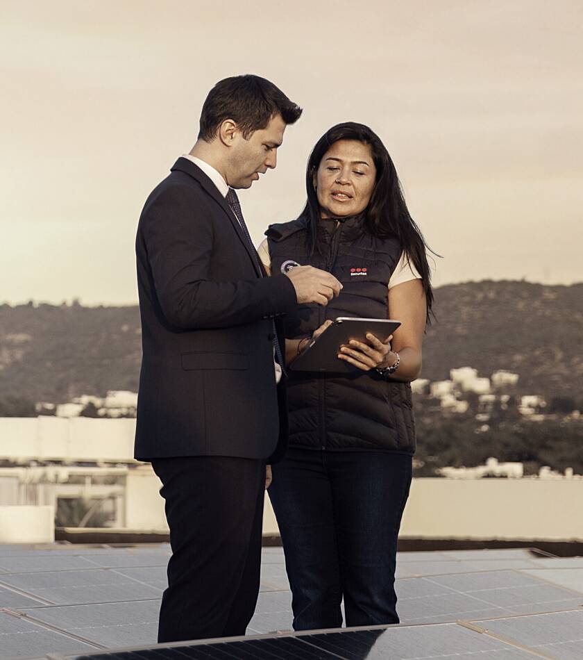 Securitas employee standing in a security operations centre, holding a tablet with multiple monitoring screens displayed behind.
