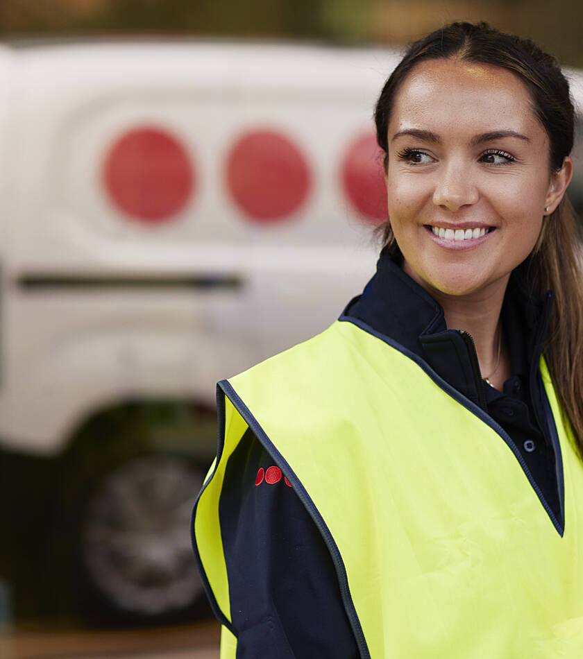 Securitas employee wearing a high‑visibility vest stands at the entrance of a facility, with a Securitas vehicle visible in the background.