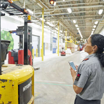 Female security officer with mobile phone looking at forklift inside a warehouse