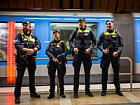 Four Münchner U-Bahnwache guards standing on a platform with a train going past in the background.