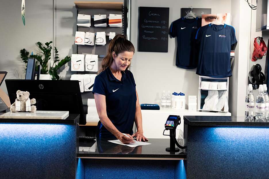 En kvindelig receptionist står i receptionen i et træningscenter