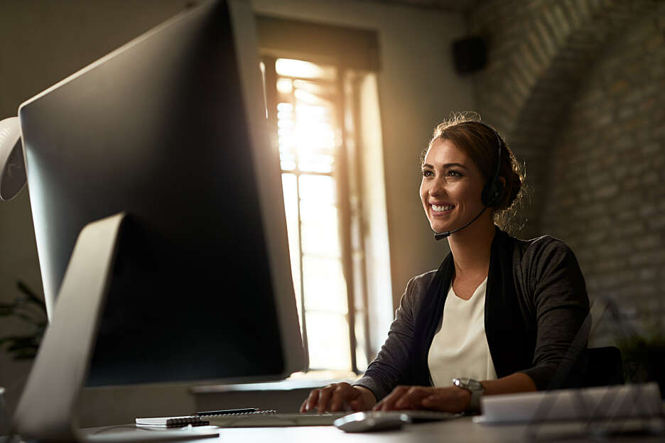Person wearing a headset and seated at a desk, working on a computer in an office environment.