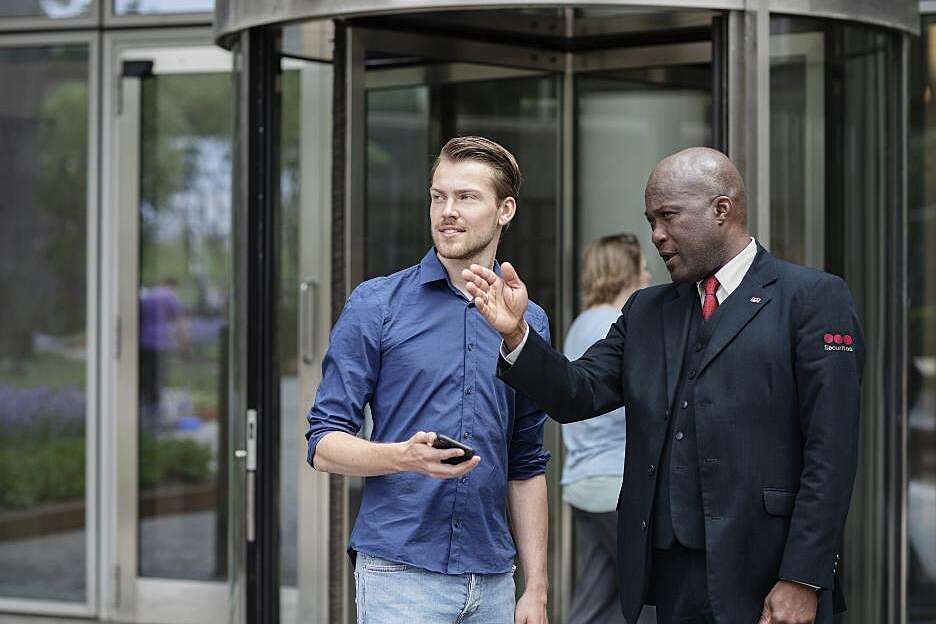 Male Securitas receptionist assists a male visitor in an office building. 