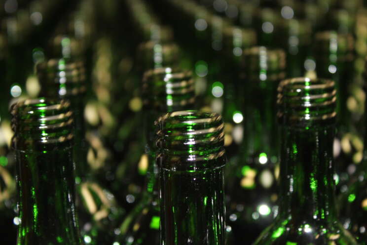 Tæt på grønne glasflasker i stor mængde, der reflekterer lys med fokus på flaskehalse.