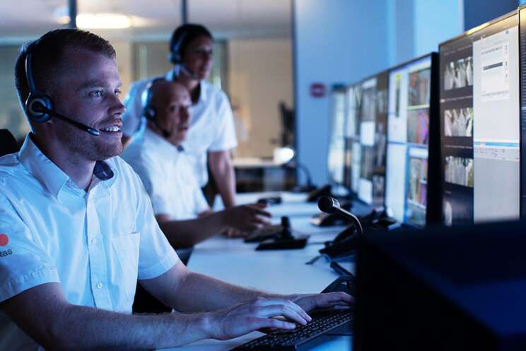 Securitas overvågningspersonale arbejder ved computere i et mørkt kontrollrum, overvåger flere skærme for sikkerhed.