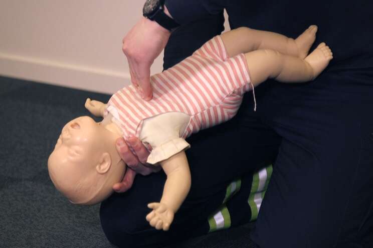 En man instruerar hur man hanterar luftvägsstopp på ett spädbarn genom en liten docka