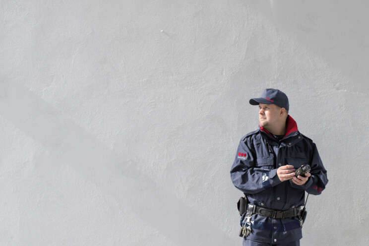 Mandlig Securitas-vagt i uniform foran en mørkegrå væg