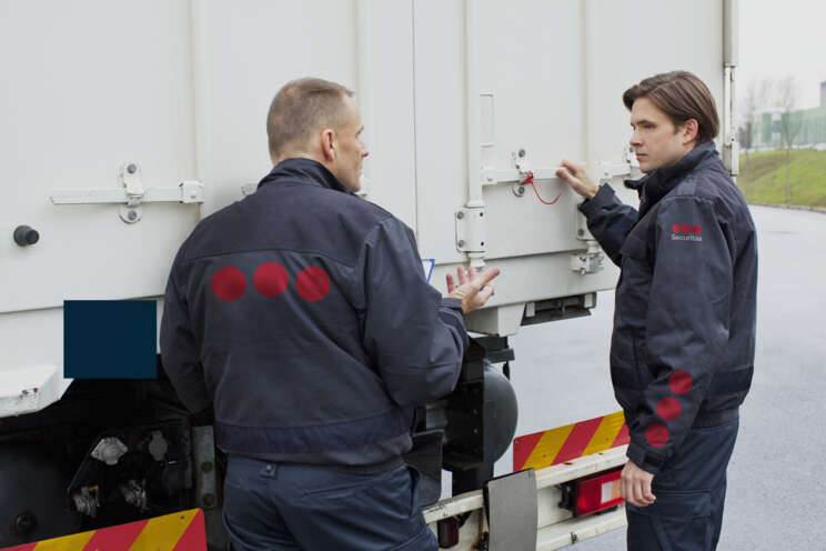 Dwoje pracowników ochrony Securitas sprawdza zabezpieczenia przyczepy ciężarówki.