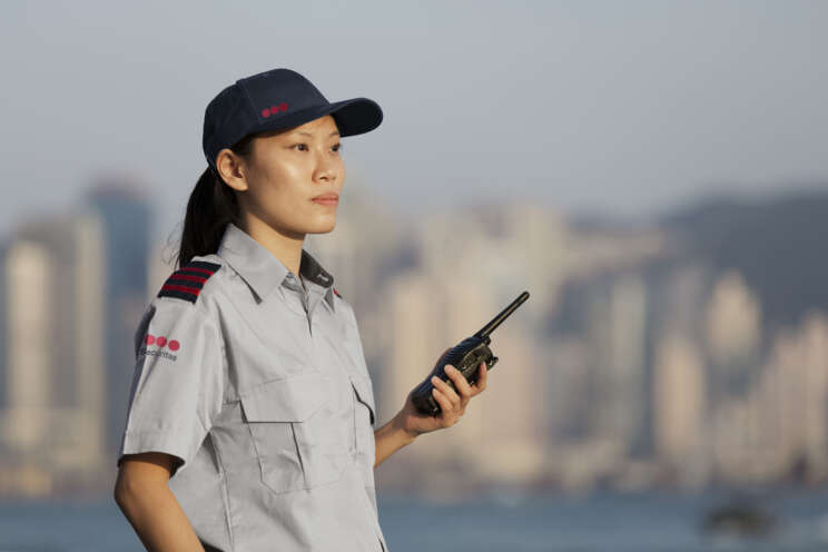 Securitas sikkerhedsvagt i uniform med kasket holder en walkie-talkie foran en byskyline.