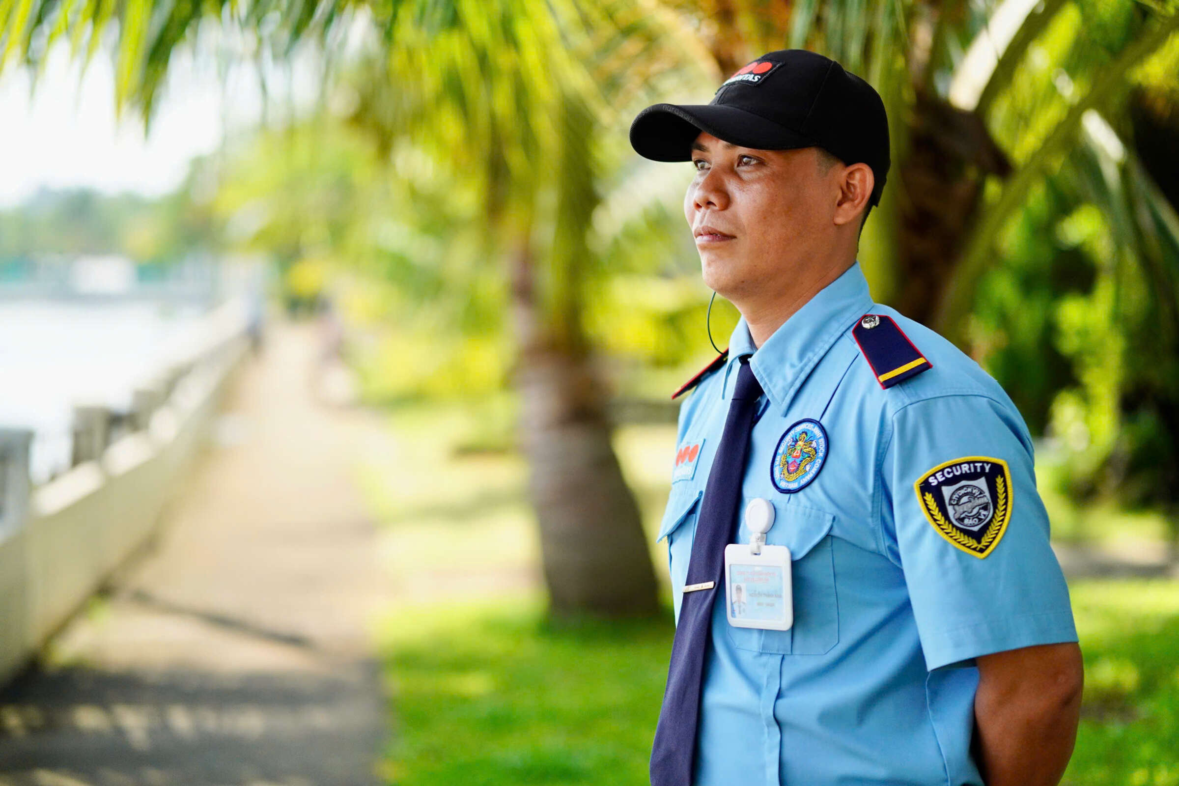 Petugas keamanan Securitas dengan seragam biru muda dan topi hitam berdiri di luar ruangan